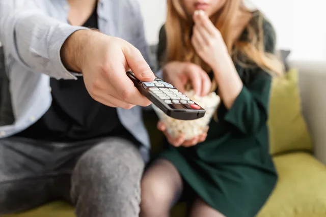 A couple enjoying a relaxing movie night, sitting on a sofa with popcorn and a TV remote. Choosing contextual programmes or audience segments for CTV